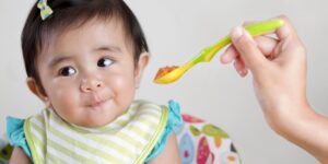 Baby in a bib turning away from a spoonful of food