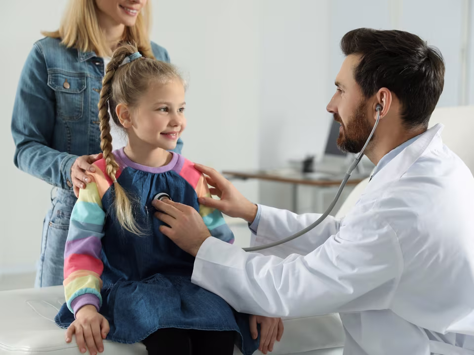 A paediatrician gently examining a smiling child with a stethoscope while her mother watches — a typical consultation at Bright Futures Health